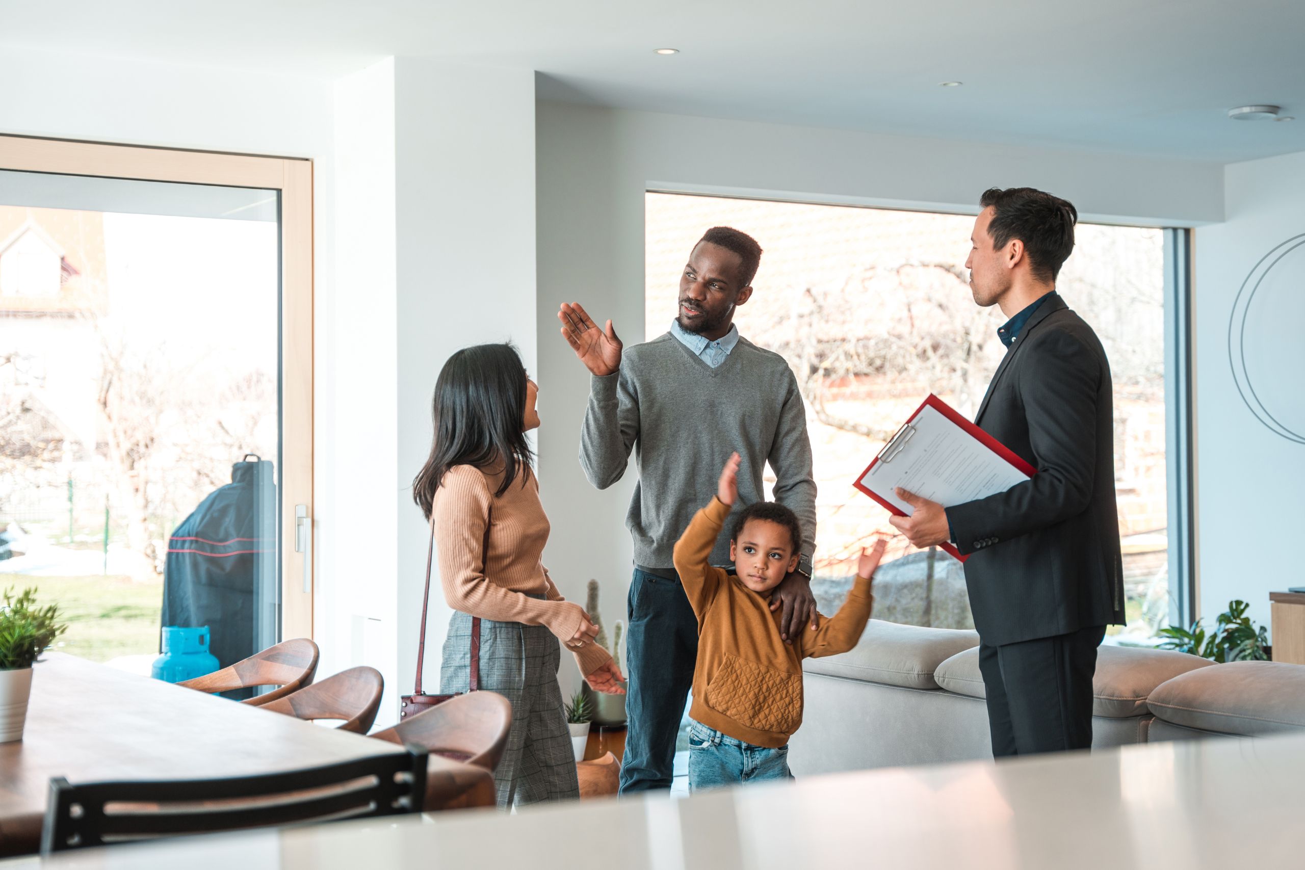 A family with a child talking to a real estate agent inside a modern home, suggesting a home tour or consultation.